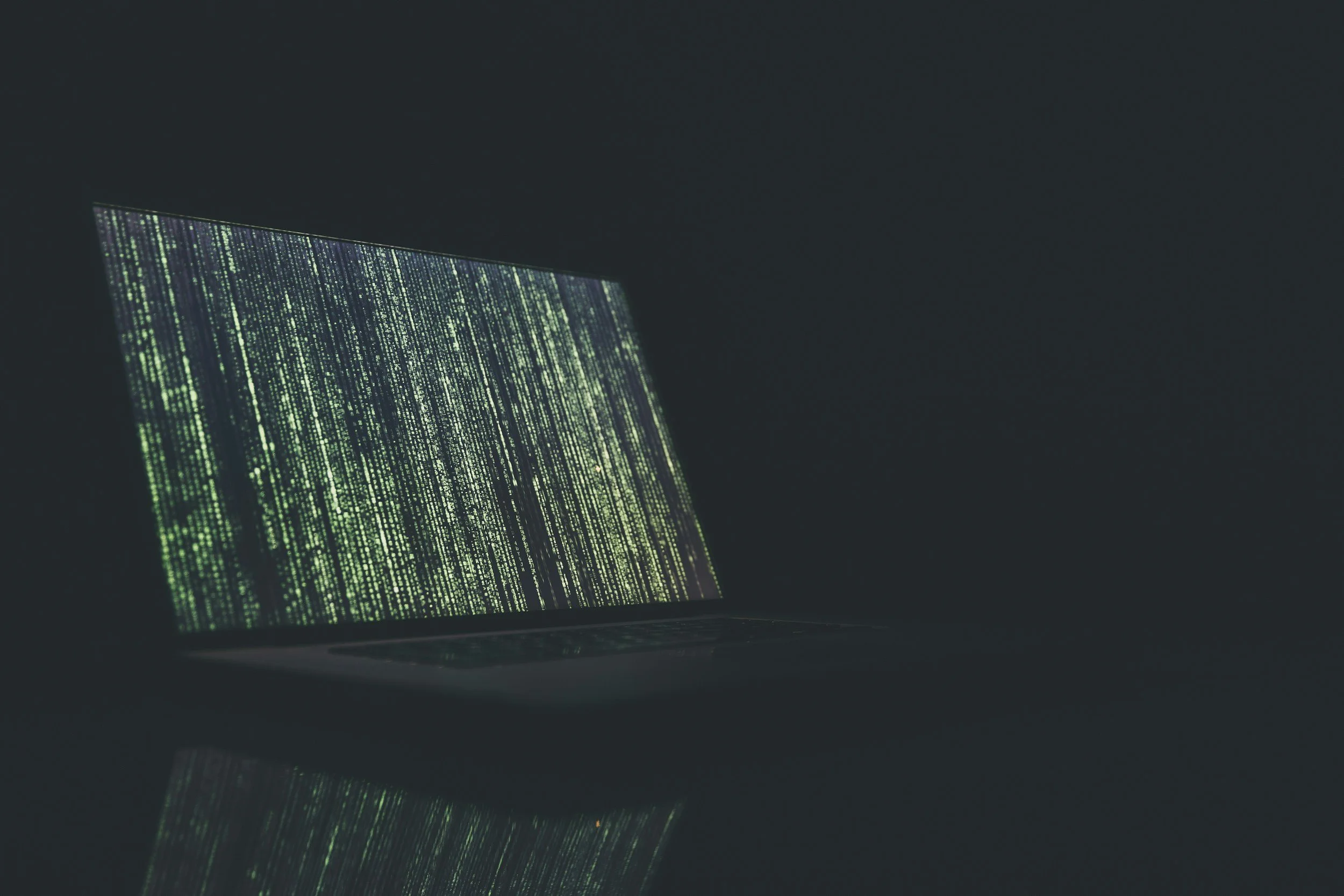 Laptop screen displaying cascading lines of code in a dark room